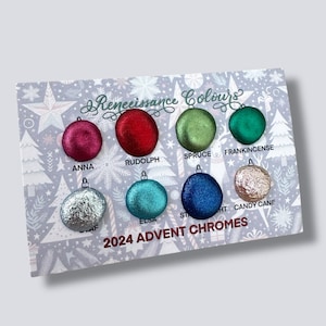 May include: A palette of eight shimmering, round, Christmas-themed colours, including Anna, Rudolph, Spruce, and Frankincense. The palette is labelled "2024 Advent Chromes" and features the text "Renaissance Colours" in a decorative font. The colours are arranged on a light grey background.