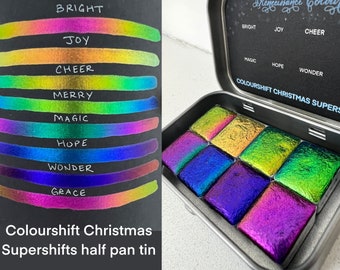 May include: A half pan tin of watercolor paints with a color shift effect. The tin is open and shows the 8 different colors: Bright, Joy, Cheer, Merry, Magic, Hope, Wonder, and Grace. The colors are iridescent and shift from one color to another depending on the angle of light.
