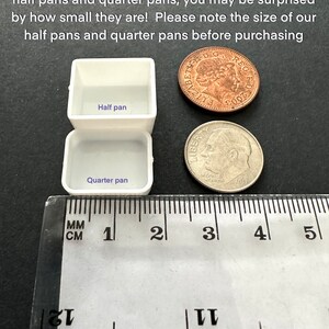 May include: Two white watercolour paint pans, labelled "Half pan" and "Quarter pan", are shown next to a ruler and two UK coins. The ruler measures 5 centimetres.