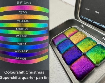 May include: A tin of iridescent watercolor paints in a quarter pan format. The tin is labeled "Colourshift Christmas Supershifts quarter pan tin". The paint colors are labeled "Bright", "Joy", "Cheer", "Merry", "Magic", "Hope", "Wonder", and "Grace".