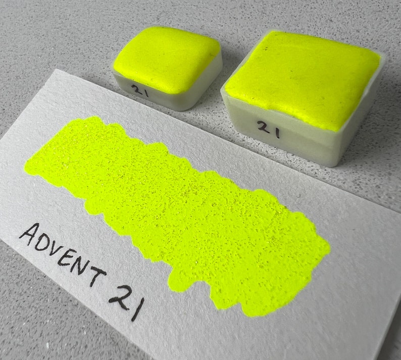 May include: A bright yellow watercolour paint pan labelled "Advent 21" with a smaller pan of the same colour and label in the background.