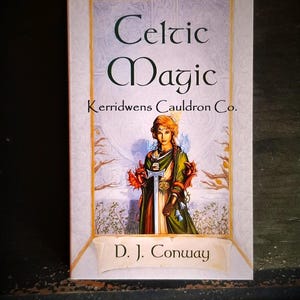 May include: A book cover with a white background and gold trim. The title is "Celtic Magic" with the subtitle "Kerridwens Cauldron Co."  The cover features a woman in a green dress holding a sword and two red dragons. The author is D.J. Conway.