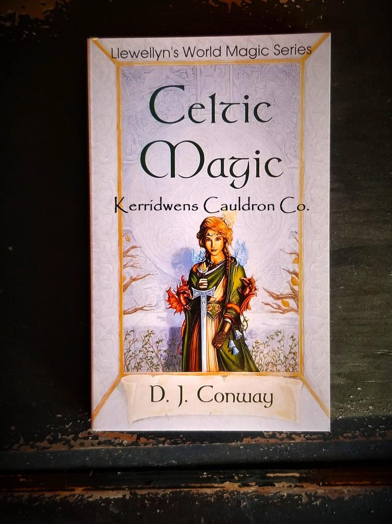 May include: A book cover with a white background and gold trim. The title is "Celtic Magic" with the subtitle "Kerridwens Cauldron Co."  The cover features a woman in a green dress holding a sword and two red dragons. The author is D.J. Conway.