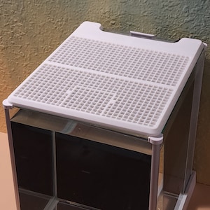 May include: White plastic reptile tank lid with a grid pattern. The lid is on top of a glass tank.