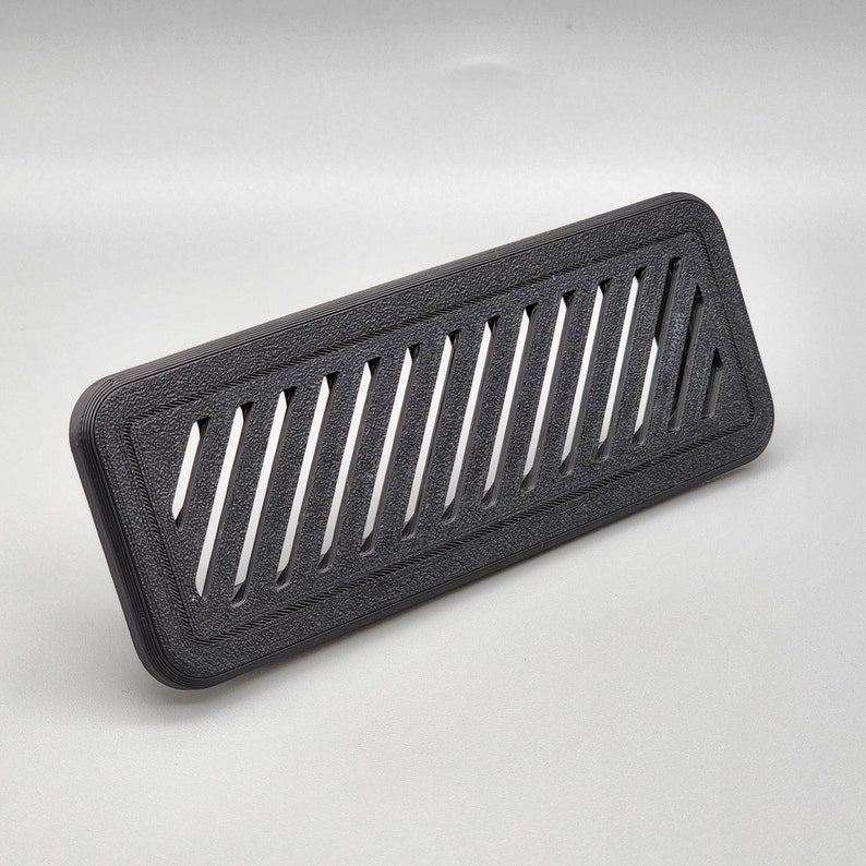 Puede incluir: Una rejilla de ventilaci&oacute;n de pl&aacute;stico negro rectangular con una serie de ranuras diagonales.