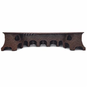 May include: A dark brown, textured bridge-shaped object featuring a series of arched openings along its length. The structure has a wide, flat top surface and flared ends, with a rough, wood-like finish across its entire exterior surface.