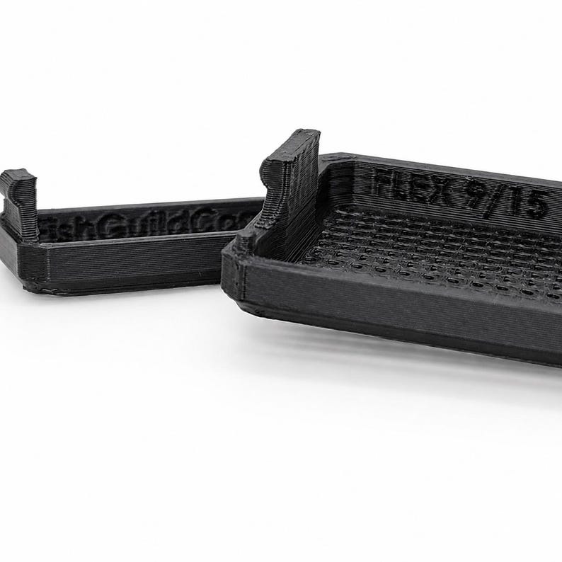 May include: A black 3D-printed rectangular tray with a grid-patterned base and raised edges. The side features the embossed text "FLEX 9/15" and "FishGuildCo". The object has a layered texture characteristic of additive manufacturing processes.