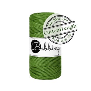 May include: A spool of olive green macrame cord wrapped in a white paper label with the text Bobbiny. A circular overlay displays the text Custom Length with measurements of 5m, 10m, 25m, 16.4 ft, 32.8 ft, and 82 ft for various cord options.