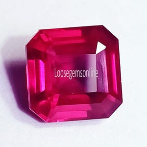 May include: A vibrant, rectangular, faceted gemstone in a deep magenta-pink hue. The stone features a clear, polished surface with sharp geometric edges and a distinct emerald cut. The text Loosegemsonline is printed in white across the centre.