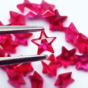 Peut inclure: Une collection de petites perles translucides en forme d'étoile rose vif avec des surfaces à facettes. Une perle étoile individuelle est tenue par une pince en métal, mettant en valeur son design à cinq branches et son aspect brillant.