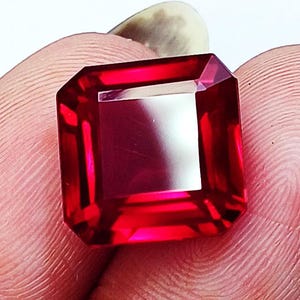 以下が含まれることがあります： 鮮やかな深紅色のスクエアカットが施されたファセットカットの宝石。鋭いエッジを持つ研磨された表面と、光を反射する透明度の高い幾何学的なファセットが特徴で、鮮やかなクリムゾンカラーを際立たせています。
