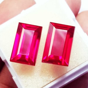 以下が含まれることがあります： 鮮やかなピンクがかった赤色の長方形のファセットカットされた宝石2つが並んでいます。それぞれの石は、透明で磨かれた表面と鋭いエッジを持ち、輝きのある反射品質で、全体に深く飽和した色合いを表現しています。