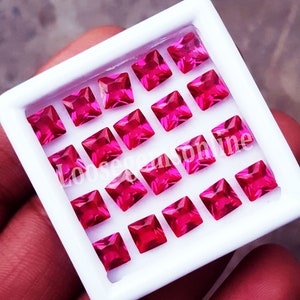 May include: A collection of square-cut, vibrant pink gemstones arranged in a white tray. The gems are evenly spaced, showcasing their facets and color. The text "Loosegemsonline" is partially visible.