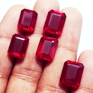 Puede incluir: Cinco piedras preciosas de color rojo vibrante, cada una tallada en forma de esmeralda rectangular con superficies facetadas. Estas piedras sueltas exhiben un tono carmesí profundo y saturado con un acabado pulido y bordes geométricos claros.