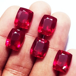 Peut inclure: Cinq pierres précieuses rouge vif, taillées en coussin avec une surface à facettes. Chaque pierre présente une teinte cramoisie profonde et saturée ainsi qu'une finition polie et réfléchissante, révélant une qualité transparente.