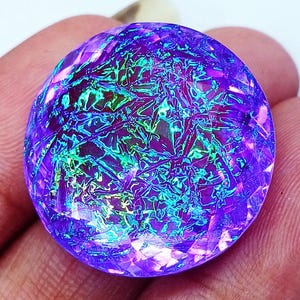 May include: A round, faceted gemstone featuring a vibrant purple base color with an iridescent, crackled internal pattern that reflects bright green and blue light across its surface, creating a multi-dimensional appearance within the circular cut.