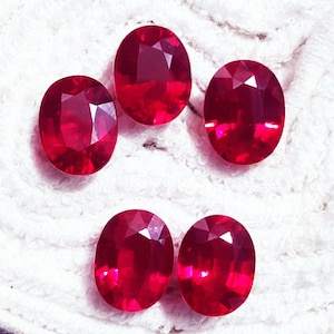 May include: Five oval-cut, deep red gemstones arranged in a cluster. Each stone features a faceted surface that reflects light, creating a brilliant appearance. The gems are uniform in shape and colour, displaying a vibrant, saturated crimson hue.