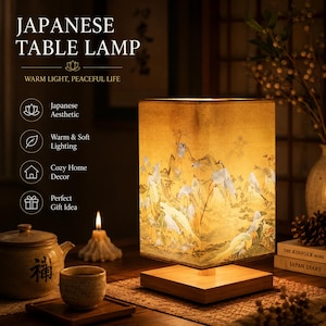 May include: A square table lamp with a wooden base and a fabric shade featuring a printed illustration of white cranes in a landscape. The lamp emits a warm, soft glow. Text on the image includes JAPANESE TABLE LAMP, WARM LIGHT, PEACEFUL LIFE.