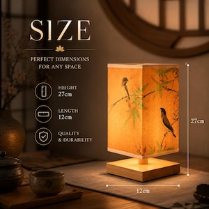May include: A rectangular table lamp with a light wood base and a fabric shade featuring a print of birds and bamboo branches. The lamp measures 27 cm in height and 12 cm in length. Text on the image includes SIZE, PERFECT DIMENSIONS FOR ANY SPACE, HEIGHT 27cm, LENGTH 12cm, and QUALITY & DURABILITY.