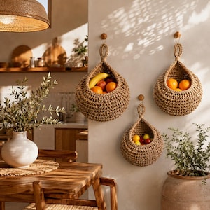 May include: Three teardrop-shaped woven baskets made of natural tan fibre, each suspended from a small wooden wall hook. The baskets contain various fresh fruits, including yellow bananas, bright orange citrus, and small red berries.