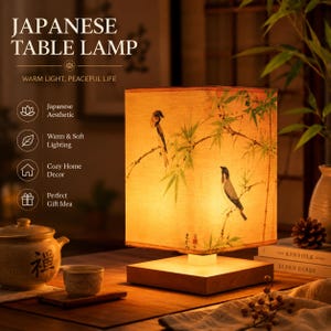May include: A square table lamp with a light-colored fabric shade featuring a printed illustration of two birds perched on bamboo branches. The lamp has a wooden base and emits a warm, soft glow. Text on the image reads: JAPANESE TABLE LAMP.