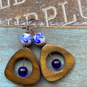 May include: A pair of earrings with a brown, triangular, geometric design. Each earring features a blue glass bead and a white bead with a blue floral design.