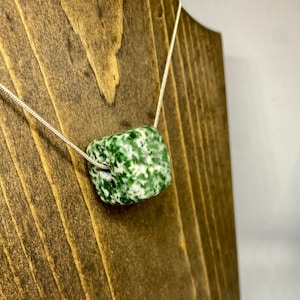 Puede incluir: Un collar de cadena de plata con un colgante cuadrado verde y blanco. El colgante está hecho de una piedra natural con un patrón de mármol.
