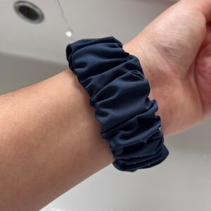 May include: A navy blue fabric watch band with a gathered, ruffled design.