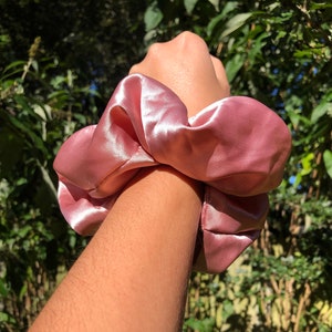May include: A pink satin scrunchie, a hair tie, with a soft, smooth texture.