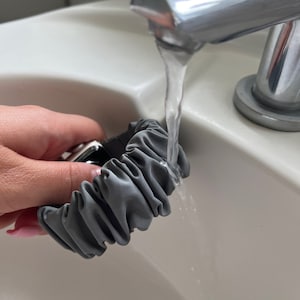 May include: A grey fabric watch band being rinsed under a tap in a white sink.