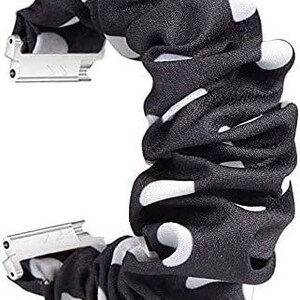 May include: A black and white polka dot scrunchie with silver metal clasps. The scrunchie is made of gathered fabric and has large white polka dots on a black background. The metal clasps are rectangular and connect the scrunchie ends.