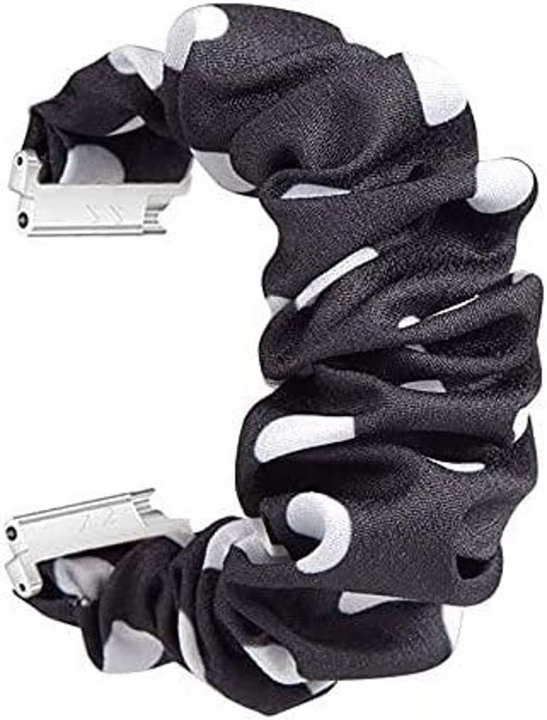 May include: A black and white polka dot scrunchie with silver metal clasps. The scrunchie is made of gathered fabric and has large white polka dots on a black background. The metal clasps are rectangular and connect the scrunchie ends.