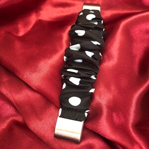 K&ouml;nnte beinhalten: Ein schwarzes und wei&szlig;es gepunktetes Stoffarmband mit einer silbernen Metallschnalle.
