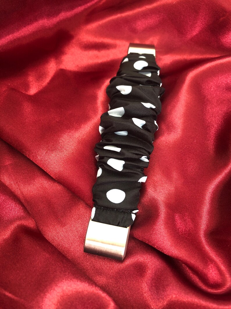 K&ouml;nnte beinhalten: Ein schwarzes und wei&szlig;es gepunktetes Stoffarmband mit einer silbernen Metallschnalle.