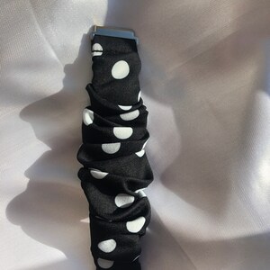 May include: Black and white polka dot watch strap with silver-coloured metal clasps. The strap is made of a ruched fabric with large white polka dots on a black background. The watch strap is shown against a white background.