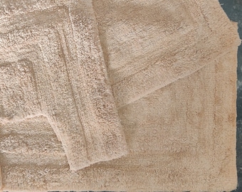 May include: Two beige bath mats, one with a square shape and the other with a rectangular shape. The mats are made of a soft, absorbent material.
