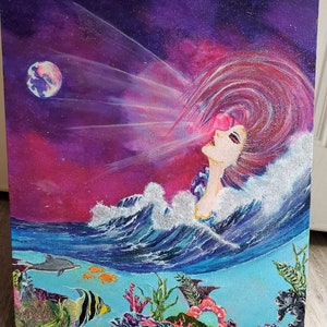 May include: A painting of a woman with long pink hair blowing in the wind, with a pink and purple galaxy behind her. The woman is surrounded by blue water with white waves and coral reefs below.