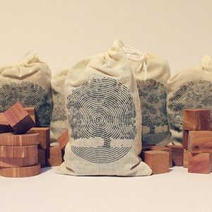 May include: Four white fabric bags with a black tree design printed on them. The bags are filled with wooden blocks of various shapes and sizes. The blocks are a reddish-brown color.
