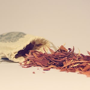 May include: A small white cloth bag with a red-brown wood chip material spilling out of it onto a white surface.