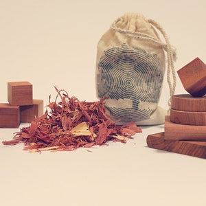 May include: A pile of red wood chips sits next to a white canvas bag with a black and white design.  The bag is tied with a white rope.  There are also several wooden blocks stacked on top of each other.