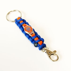 May include: A blue and orange paracord keychain with a silver clasp and a round charm with the letters "CHS" in blue on an orange background.