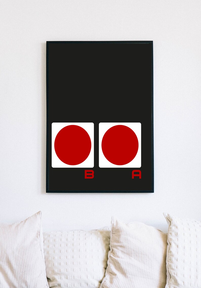 May include: Framed art print featuring a black background with two white squares, each containing a red circle. The letters "B" and "A" are in red below the squares. The artwork is displayed above white pillows.