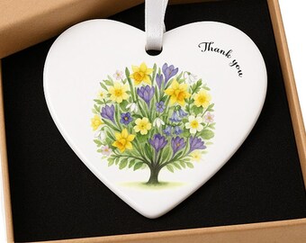 May include: A white heart-shaped ornament with a floral design in yellow, purple, and green, and the words "Thank you." The ornament hangs from a white ribbon and is presented in a brown gift box.