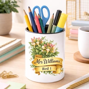 May include: White ceramic pencil holder with a black rim, filled with pencils, scissors, and a highlighter. The holder features a floral design and a gold banner with the text "Mrs Williams Red 1".