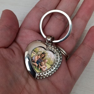 Pu&ograve; includere: Portachiavi a forma di cuore argentato con una foto di una famiglia di quattro persone. Il portachiavi ha un anello argentato e un ciondolo a forma di cuore argentato con una foto di una madre e tre figli.