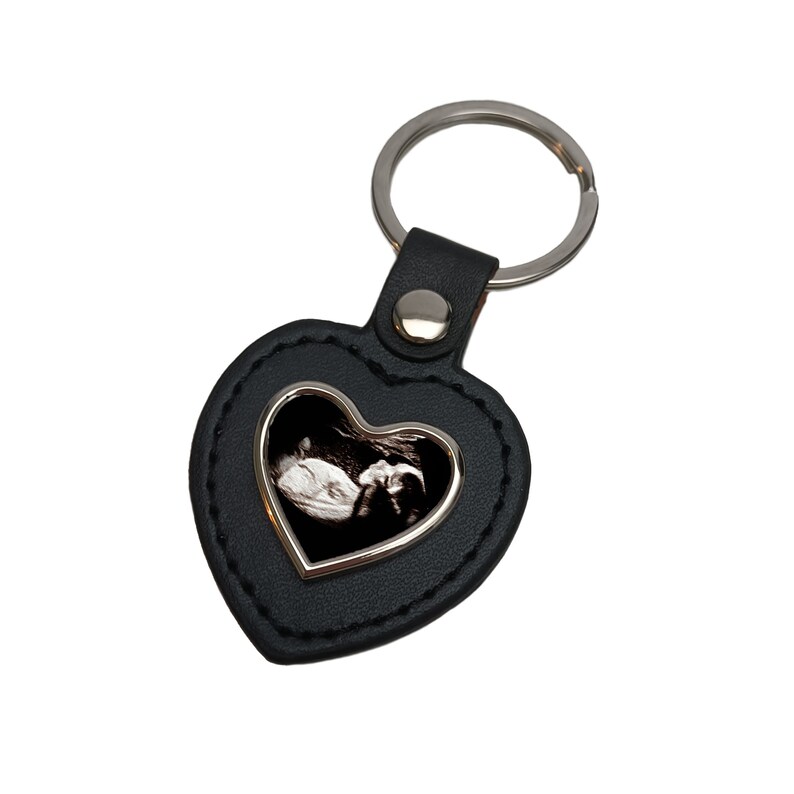May include: Black leather heart-shaped keyring with a silver frame and a black and white ultrasound image inside.