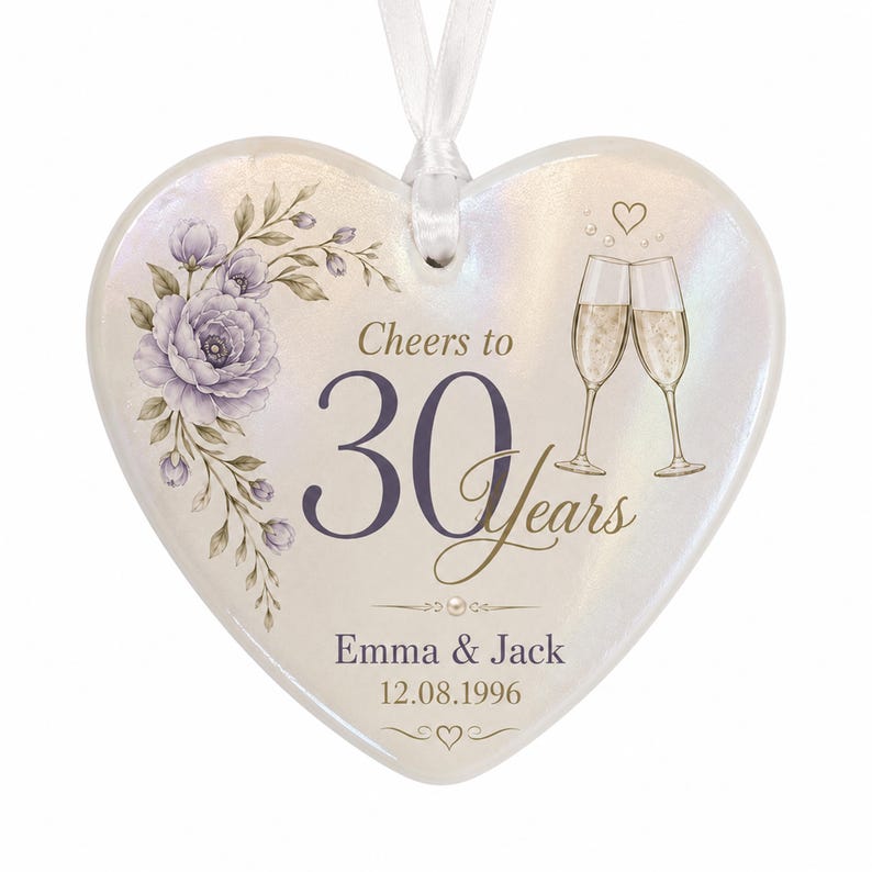 May include: A heart-shaped ceramic ornament with an iridescent finish, featuring a purple floral illustration, two champagne flutes, and the text "Cheers to 30 Years," "Emma & Jack," and "12.08.1996." A white ribbon is attached to the top for hanging.