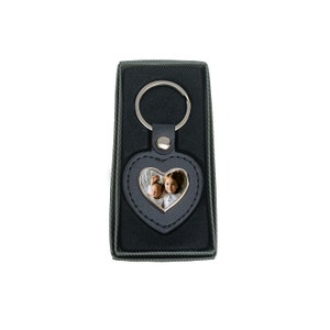 May include: A black leather heart-shaped keyring with a silver frame and a photo insert. The keyring has a silver ring and is in a black box.