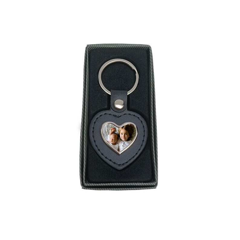 May include: A black leather heart-shaped keyring with a silver frame and a photo insert. The keyring has a silver ring and is in a black box.