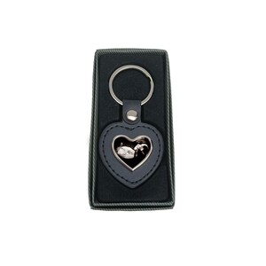 May include: A black leather heart-shaped keyring with a silver ring and a silver frame holding a black and white ultrasound image. The keyring is in a black velvet box.